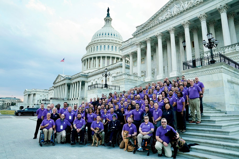 A large group wearing purple shirts poses on the steps in front of the U.S. Capitol building.