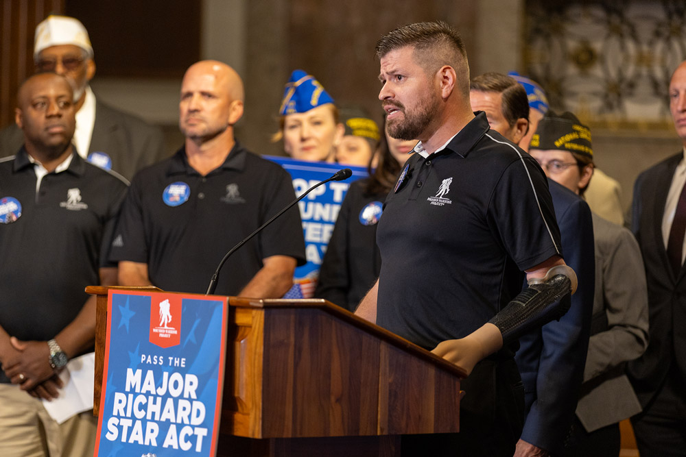 WWP VP of Government and Community Relations Jose Ramos speaks at a podium wearing a prosthetic arm during a press event supporting the Major Richard Star Act. 